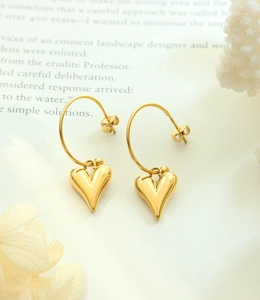 Détail de boucles d'oreilles cœur dorées avec finition poli miroir sur fond de livre ancien