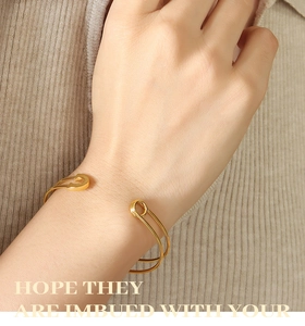 Detail of a gold safety pin style open cuff bracelet on a woman wearing a beige sweater