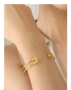 Detailed view of a gold safety pin cuff bracelet with polished finish on model wrist