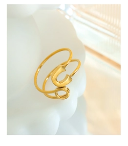 Close-up of golden U-shaped double-layered open ring on a wavy white textured surface