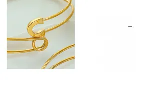 Detail of 18K gold safety pin cuff bracelet with a stylish letter C emblem detail