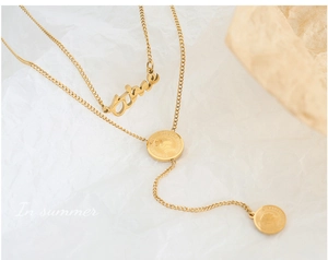 Détail d'un collier double épaisseur doré avec pendentif lettre et médailles gravées