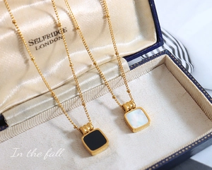 Detail of square black and white pendants on golden ball chains in a blue jewelry box