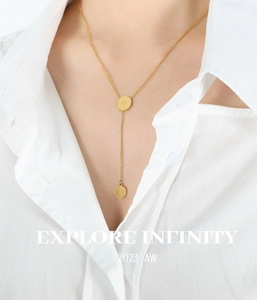 Gros plan d'un collier à double pendentif en or porté par un mannequin en chemise blanche