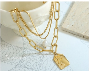 Close-up of triple-layered gold necklace with square relief pendant and freshwater pearl