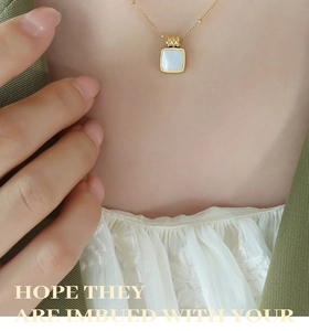 Close-up of golden square necklace with white mother-of-pearl inlay worn by a model