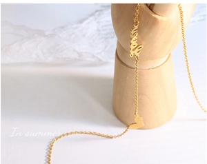 Close-up of golden necklace with delicate heart and cursive love pendant on wood mannequin