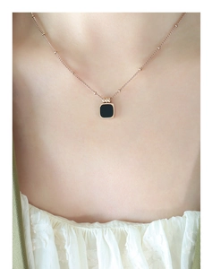 Close-up of a square black pendant necklace with gold plating worn by a female model