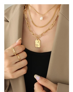 Close-up of layered gold necklaces with pearl and relief pendant on model with rings