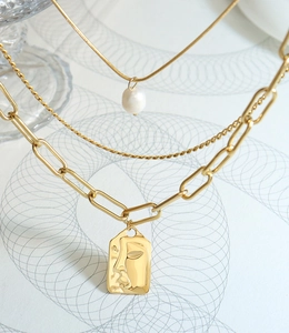 Detailed close-up of triple-layered golden necklace with pearl and portrait pendant