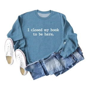 Flat lay of blue sweatshirt with 'I closed my book to be here' text and denim jeans