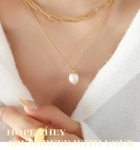 Détail de colliers en couches dorées avec pendentif perle d'eau douce sur un pull doux