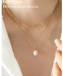 Gros plan sur le collier double épingle à nourrice doré avec pendentif perle baroque