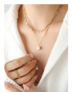 Détail du collier chaîne dorée multicouche avec perle d'eau douce sur un pull blanc