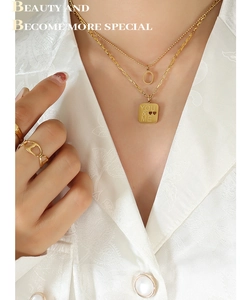 Detail of layered gold titanium necklace with engraved YOU & ME square pendant and rings