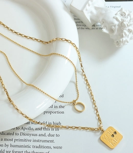 Detail of layered gold necklaces with You & Me pendant and hollow heart charms