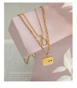 Detail of double-layer gold necklace with YOU & ME engraved square pendant on a display stand