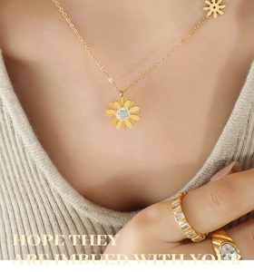 Détail du collier marguerite dorée avec zircons porté sur un pull en maille beige