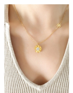 Gros plan d'un collier pendentif marguerite dorée avec zircons sur un pull en maille beige