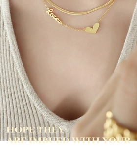 Detail of layered gold snake chain and Love heart pendant on cream cardigan