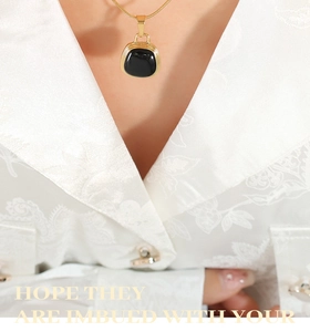Detail of a gold snake chain necklace with a black rectangular pendant on a model