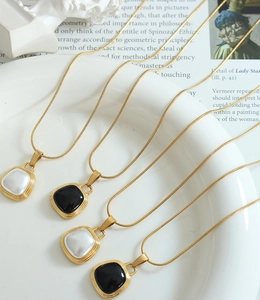 Detail of square black enamel and white pearl pendants on golden snake chain necklaces