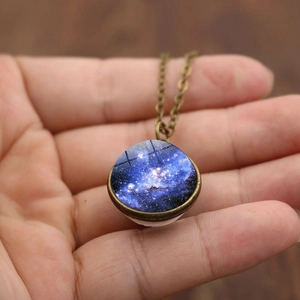 Détail du pendentif sphère de verre galaxie tenu à la main avec chaîne en bronze