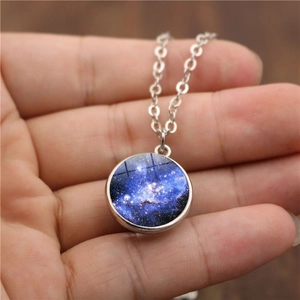 Gros plan d'un pendentif boule de verre galaxie bleue tenu à la main sur une chaîne