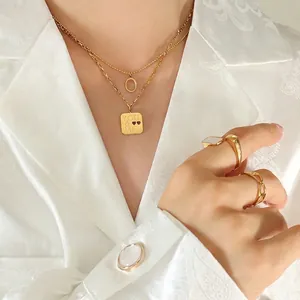 Gold layered necklace set with letter pendant on model wearing white jacquard blazer