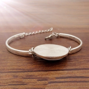 Detailed view of silver charm bracelet base with sunburst texture on wooden background
