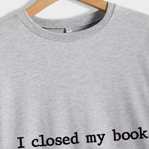 Gray crewneck sweatshirt with 'I closed my book' print hanging on wooden hanger