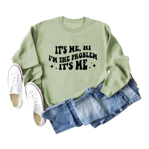 Salbeigrüner Pullover mit schwarzem Slogan-Text flach liegend mit Jeans und Schuhen