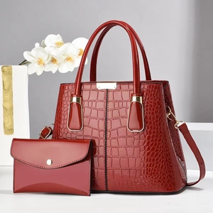Detalle de bolso rojo oscuro en charol con grabado de cocodrilo y metal dorado