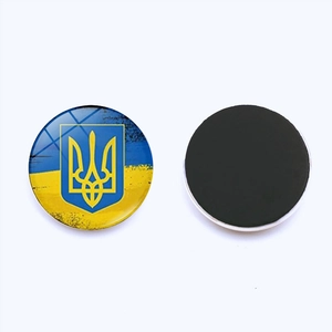 Round Ukraine flag and trident glass magnet with black magnetic backing on white surface