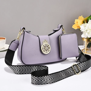 Detalle del bolso de hombro lila en piel granulada con emblema dorado y correa ancha