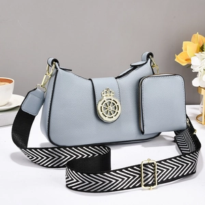 Bolso bandolera azul niebla con diseño de lichi, emblema dorado y correa tejida