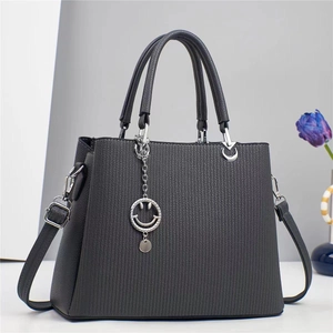 Detail of dark grey striped handbag featuring dual handles and silver smiley face charm