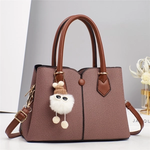 Detail view of pink textured fabric tote bag with brown leather handles and plush pendant