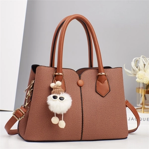Detail of tan textured tote bag with cute white plush charm and gold hardware strap