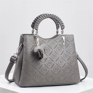 Detalle de bolso gris grabado con asa trenzada y un bonito colgante de elefante de cuero