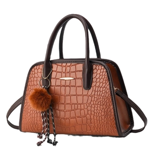 Braune Handtasche mit Krokodilmuster, Doppelgriffen und flauschigem Anhänger auf Weiß