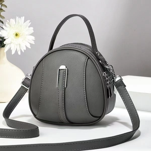Detail of grey circular crossbody bag with pebbled leather texture and double zippers