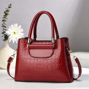 Close-up of red crocodile-embossed leather handbag with gold hardware and top handles