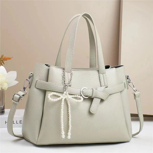 Detail of light green litchi grain leather handbag with pearl bow charm and metal buckle