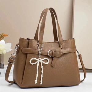 Detail of brown litchi grain leather tote with white pearl bow charm and silver buckle
