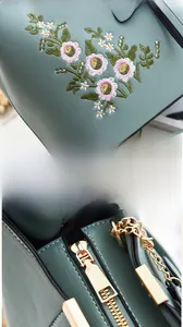 Détail de la broderie florale et des finitions métalliques dorées sur le sac à main vert