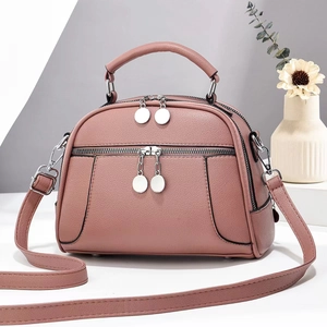 Détail du sac à main en cuir rose poudré avec double fermeture éclair et pendentif rond