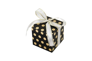 Macro view of a square black gift box with gold dots and a white ribbon bow detail