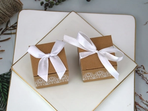 Close-up of square kraft paper candy boxes with white lace prints and satin ribbons