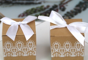 Close-up of square kraft paper candy boxes with white lace print and satin bow